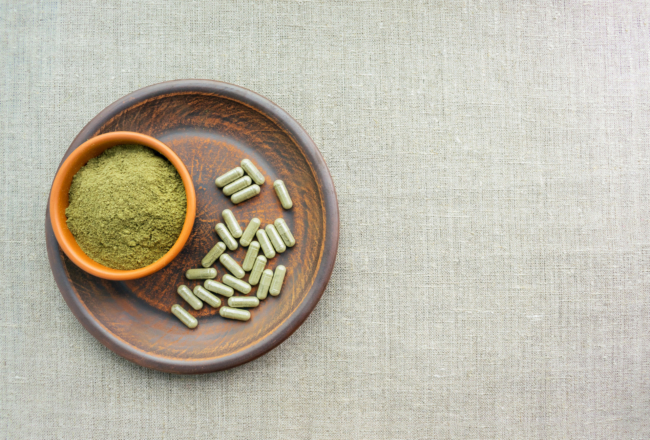 Supplement kratom green capsules and powder on brown plate. Herb Just added Jong Kongs and Bali's to the capsule menu!!!